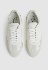 Sneakers bianchi che presentano una combinazione di materiali lisci e testurizzati, accenti grigi, punta rotonda e lacci. Design minimalista.