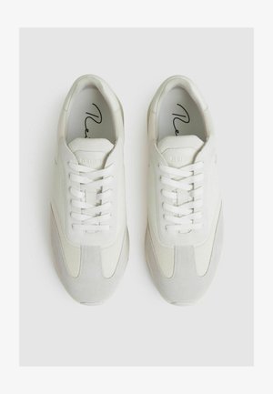 Biele tenisky s kombináciou hladkých a textúrovaných materiálov, so sivými akcentmi, okrúhlou špičkou a šnúrkami. Minimalistický dizajn.