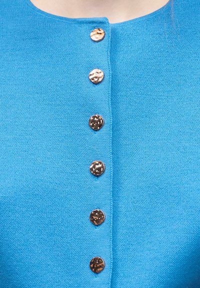 Μπλε πλεκτό ένδυμα με έξι στρογγυλά, υφασμάτινα μεταλλικά κουμπιά κατά μήκος της μπροστινής περιοχής του λαιμού.
