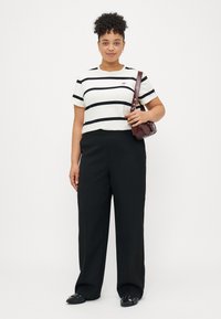 Fehér, rövid ujjú póló fekete vízszintes csíkokkal, laza fekete nadrággal párosítva. Kiegészítők között egy kis bordó táska és fekete cipő található.