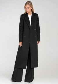 Czarny podwójnie zapinany płaszcz z długimi rękawami, wykonany z teksturowanej tkaniny i dopasowanym kroju, z dwoma dużymi guzikami i długością do kolan.