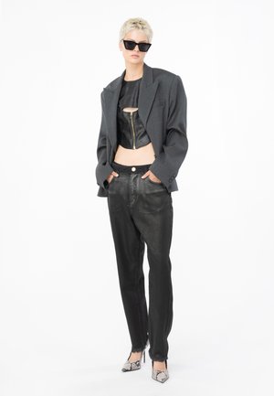 Top in pelle nera corta con zip frontale, giacca grigia oversize e pantaloni neri. Completato con scarpe con tacco alto a fantasia.