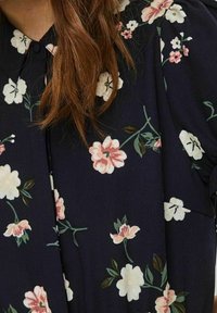 Dunkelblaue Bluse mit Blumenmustern in Pink, Weiß und Grün. Das Material wirkt leicht und weich, mit Knopfleiste.