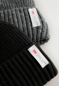 Două căciuli tricotate cu nervuri, una gri închis și alta neagră, având etichete 3M Thinsulate. Materiale texturate cu un aspect confortabil și cald.