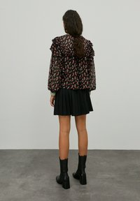 Zwarte bloemenblouse met gerimpelde mouwen, gecombineerd met een geplooide zwarte rok en zwarte hakken enkellaarsjes.