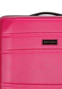 Valigia rigida rosa con superficie testurizzata, dotata di tre scanalature orizzontali e di una maniglia superiore nera. Etichetta del marchio: WITTCHEN.