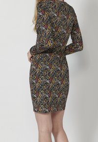 Sukienka z długim rękawem o dopasowanym fasonie, wykonana z czarnego materiału zdobionego kolorowymi wzorami kwiatowymi w odcieniach czerwieni, żółci i bieli.