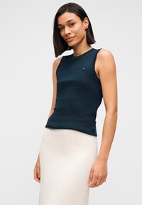 Σκούρο ναυτικό αμάνικο τοπ από ριπ ύφασμα, με στρογγυλή λαιμόκοψη και μικρή λεπτομέρεια λογότυπου στο στήθος. Συνδυασμένο με ανοιχτόχρωμη φούστα με υφή.