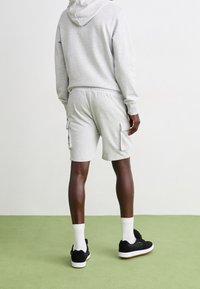 Harmaa huppari ja siihen sopivat cargo-shortsit, joissa on sivutaskut. Valkoiset sukat ja mustat lenkkarit. Sujuva materiaali, rento muotoilu. Neutraali tausta.