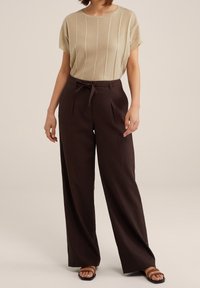 Beige kortärmad stickad topp med vertikala ränder, tillsammans med högmidjade vida mörkbruna byxor med knytband i midjan.