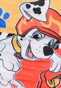 Perro dálmata blanco sonriente en un dibujo animado, usando un casco naranja de bombero y sosteniendo un objeto rojo, con una huella de pata azul de fondo.