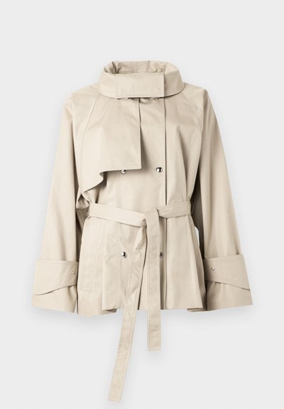 Μπεζ κοντό παλτό τύπου trench με ψηλό γιακά, διπλό κούμπωμα με κουμπιά snap, μακριά μανίκια, φαρδιά μανσέτα, τσέπες μπροστά και ζώνη μέσης δεμένη.