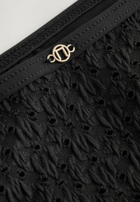 Krupan plan crne teksturirane tkanine s malim rupicama, prošivenim rubovima i zlatnim okruglim metalnim kopčom na crnoj elastičnoj traci.