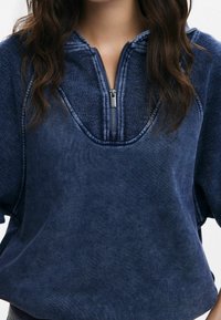 Felpa cropped blu navy con chiusura a zip, caratterizzata da un tessuto testurizzato e maniche larghe. Il collo ha un design a V profonda.