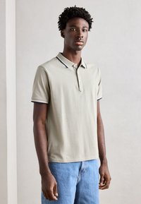 Cămașă polo dintr-un material gri deschis, cu m�âneci scurte, având un guler cu margine albastră și trei nasturi, asortată cu blugi din denim albastru.