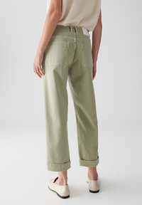 Pantalons verts à taille haute, larges, avec bas retroussés et poches arrière ; en coton, présentant une texture lisse et une ceinture de contraste neutre.
