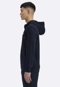 Granatowa bluza z kapturem z mieszanki bawełny, z przednią kieszenią, kapturem z troczkami oraz ściągaczami na rękawach z białymi akcentami.