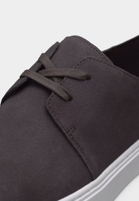 Σκούρο γκρι αθλητικό παπούτσι από σουέντ με κορδόνια στο ίδιο χρώμα και λευκή ελαστική σόλα, με εμφανή ραφές και υφή.