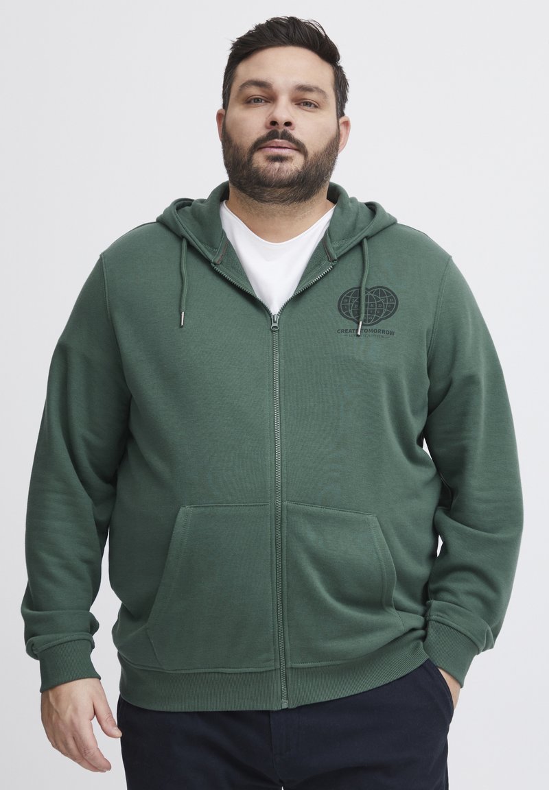 Felpa verde con zip realizzata in tessuto morbido, dotata di tasca frontale e cappuccio con cordino. Include un piccolo logo nella zona sinistra del petto.