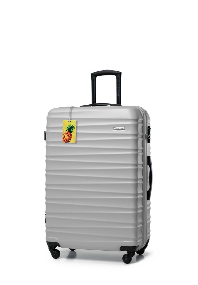 Srebrna twarda walizka z żłobioną powierzchnią, wysuwaną rączką, czarnymi kółkami i kolorową metką do bagażu w kształcie ananasa.