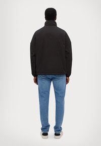 Sort isoleret jakke med høj krave, løs pasform og dropped shoulders, parret med lyseblå denim jeans og hvide sneakers.