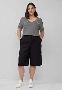 Czarne spodenki 3/4 z elastycznym paskiem, w zestawieniu z krótkim rękawem czarno-białą pasiastą koszulką typu V-neck z małym logo.