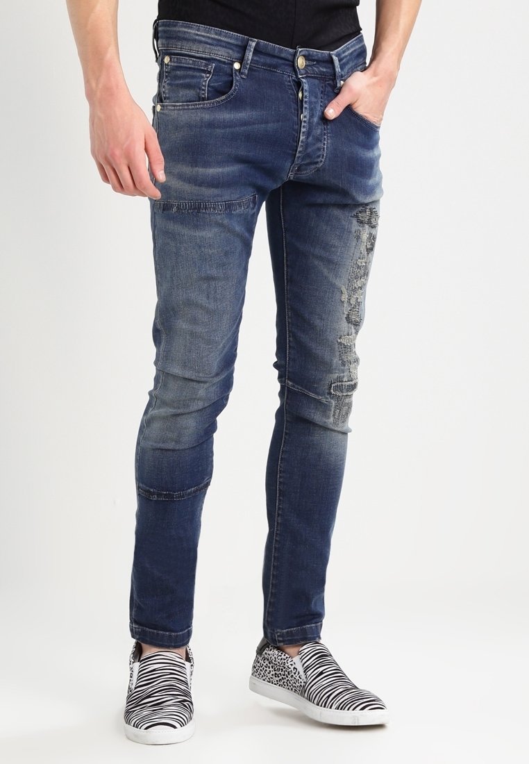 Persona che indossa jeans slim-fit blu sbiaditi con dettagli strappati e scarpe slip-on bianco e nere con stampe zebrate e leopardate.