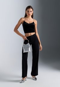 Top corto de terciopelo negro, pantalones ajustados negros, bolso de mano de lentejuelas plateadas con un asa circular y zapatos planos plateados con punta afilada y correas.
