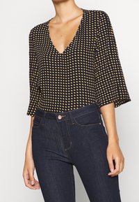 Marinblus med gula prickar, V-ringning och trekvartsärmar, i kombination med mörka denimjeans med klassisk passform och framfickor.