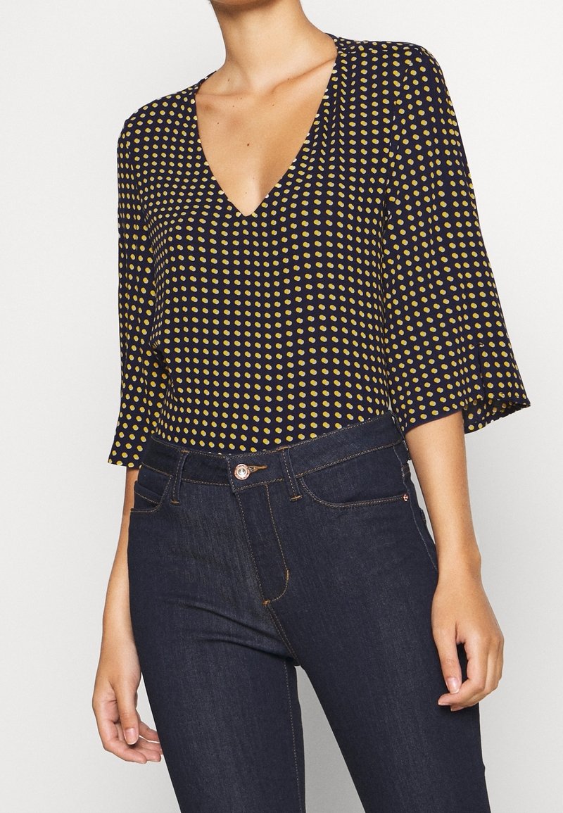 Marinblus med gula prickar, V-ringning och trekvartsärmar, i kombination med mörka denimjeans med klassisk passform och framfickor.