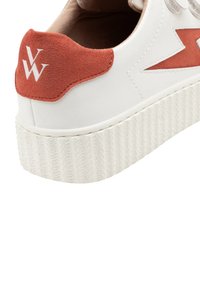 Witte sneaker met een gestructureerde rubberen zool, voorzien van een rode suède hieltab en een gedurfde witte logo aan de achterkant. Eenvoudig ontwerp met strakke lijnen.