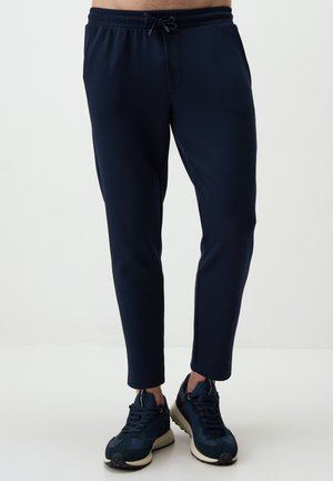 Navy jogger pants with an elastic waistband, drawstring, tapered fit, and side pockets, paired with dark sneakers.