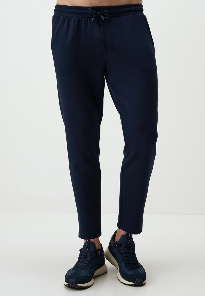 Navy Jogginghosen mit elastischem Bund, Kordelzug, schmalem Schnitt und seitlichen Taschen, kombiniert mit dunklen Sneakers.