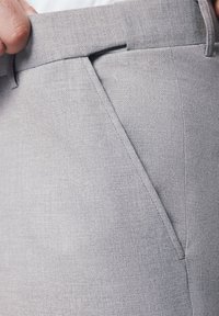 Szare spodnie z tkaniny o gładkiej fakturze, z płaskim przodem i kieszeniami po bokach. Widoczne przeszycia wzdłuż szwów.