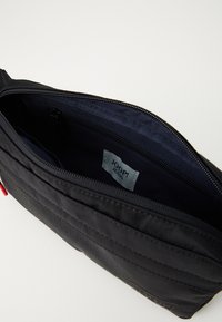 Pochette nera con zip, dotata di un vano principale aperto, tasca interna con zip e un'etichetta "JOOP! JEANS" visibile all'interno.