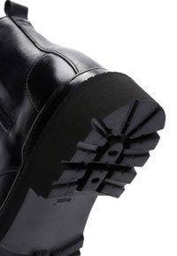 Bota de cuero negro con una suela de goma texturizada que presenta un patrón de tacos para tracción y un diseño de caña suave con detalles de costura.