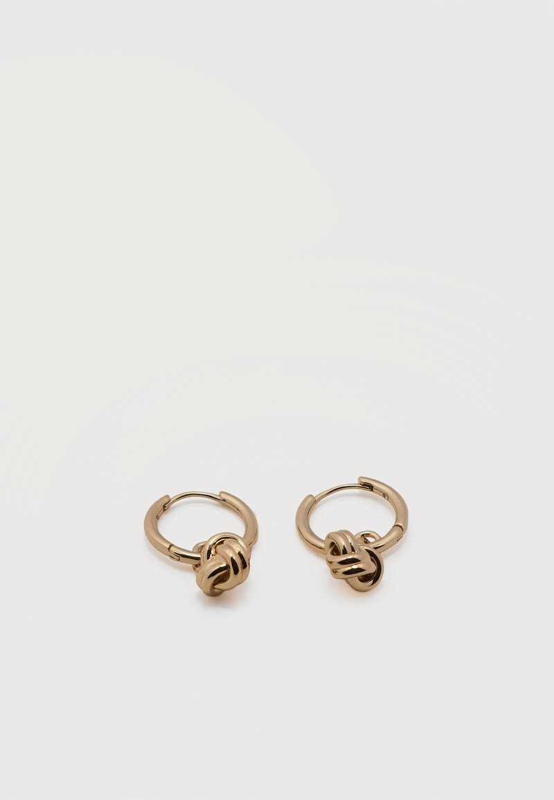 Ζευγάρι μικρών χρυσών κρίκων με λεπτομέρεια σε στριφτό κόμπο σε απλό λευκό φόντο.