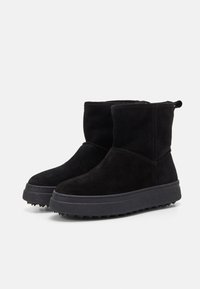 Schwarze Wildleder-Stiefeletten mit einer flachen, strukturierten Gummisohle. Sie verfügen über eine abgerundete Zehenpartie und gestickte Details. Zudem haben sie eine kleine Schlaufe auf der Rückseite.