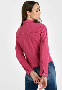 Aansluitend roze denimjack met een kraag, lange mouwen en knoopmanchetten. Beschikt over een achterzijde met yoke en subtiele stikseldetails.