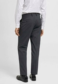 Sive hlače s krojenim rezom, s glatkom teksturom i jednim stražnjim džepom, uparenim s crnim cipelama.