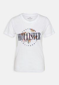 White short-sleeve cotton T-shirt with "Hollister" text, "Southern California" circular text, floral design, and orange butterflies on the front.