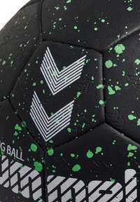 Balón de fútbol negro con patrón de salpicaduras verdes. Presenta diseños de chevrón blancos y paneles hexagonales texturizados. Material sintético duradero.
