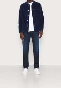 Navy corduroy jacket with silver buttons, white t-shirt, dark blue jeans, and white sneakers, shown on a neutral background.
