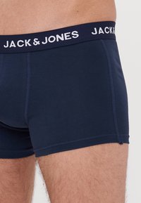 Navy blue cotton boxer shorts with elastic waistband featuring "JACK & JONES" in white text, smooth texture, fitted design, and contrast stitching.