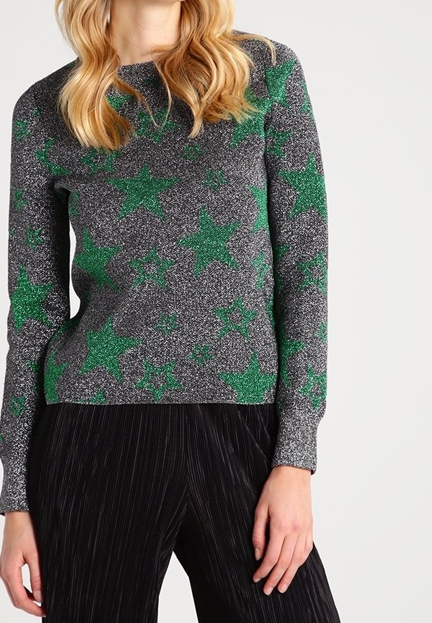 Pull en tricot gris avec des motifs d'étoiles verts et une finition texturée, associé à un pantalon noir à rayures. Manches longues et encolure ras du cou.