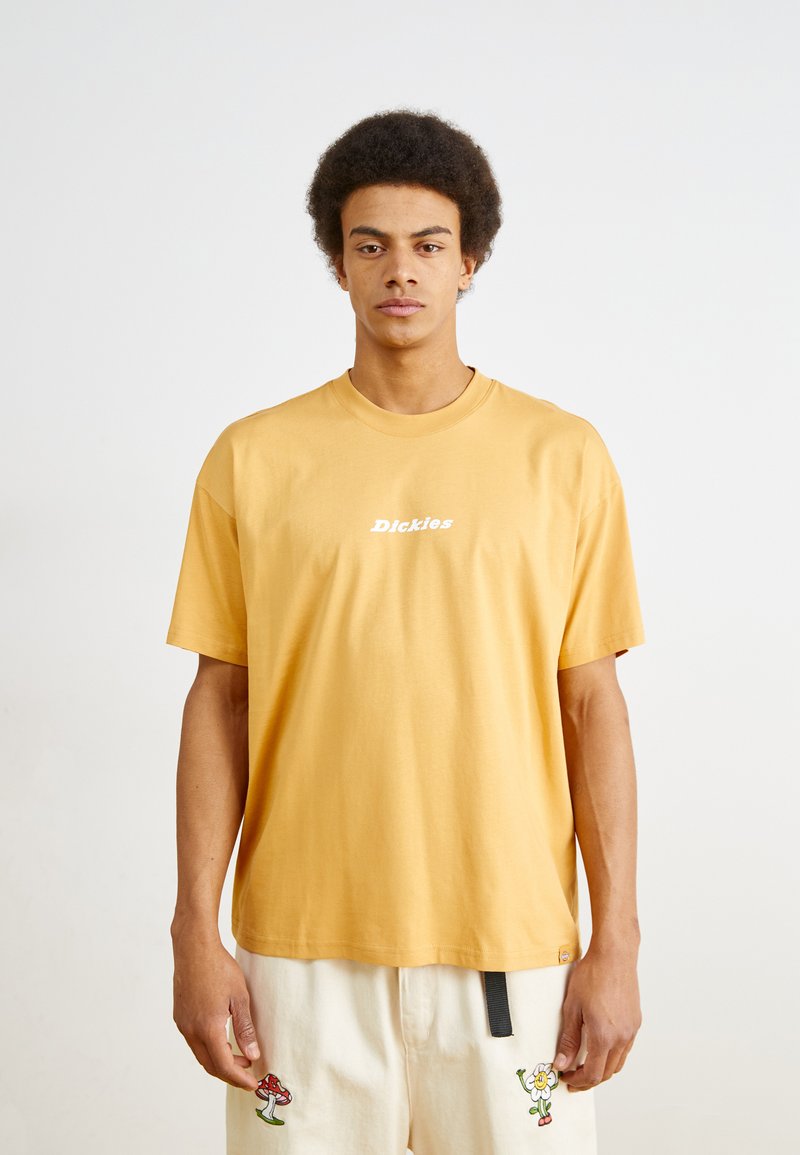Un tricou din bumbac galben cu mâneci scurte, având un logo alb pe piept. Croiala este lejeră, cu un decolteu rotund și o textură moale.