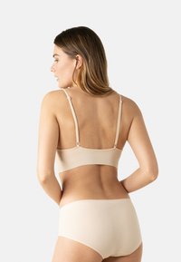 Brassière beige sans coutures avec bretelles ajustables et culotte taille haute assortie, texture douce, design minimaliste, sans éléments visibles.