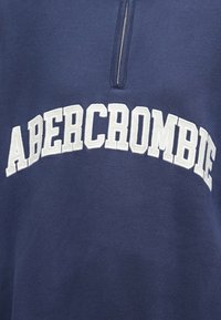 Granatowy sweatshirt z półzamkiem, na którym wyraźnie wyszyty jest biały napis "ABERCROMBIE" na klatce piersiowej. Miękka faktura materiału.
