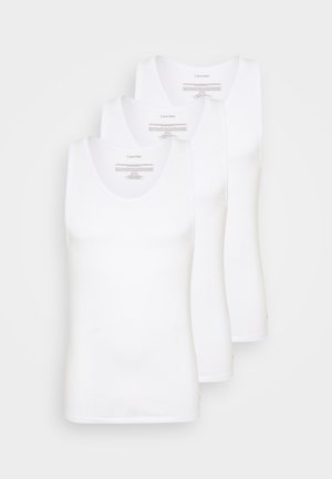 Three white cotton tank tops with rounded necklines, smooth texture, and a fitted design. Logos and care instructions visible on the back.
