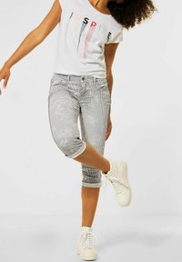 Weißes T-Shirt mit dem Aufdruck "INSPIRE", kombiniert mit grauen und weißen gestreiften cropped Hosen mit floralem Muster, getragen mit weißen High-Top-Sneakern.